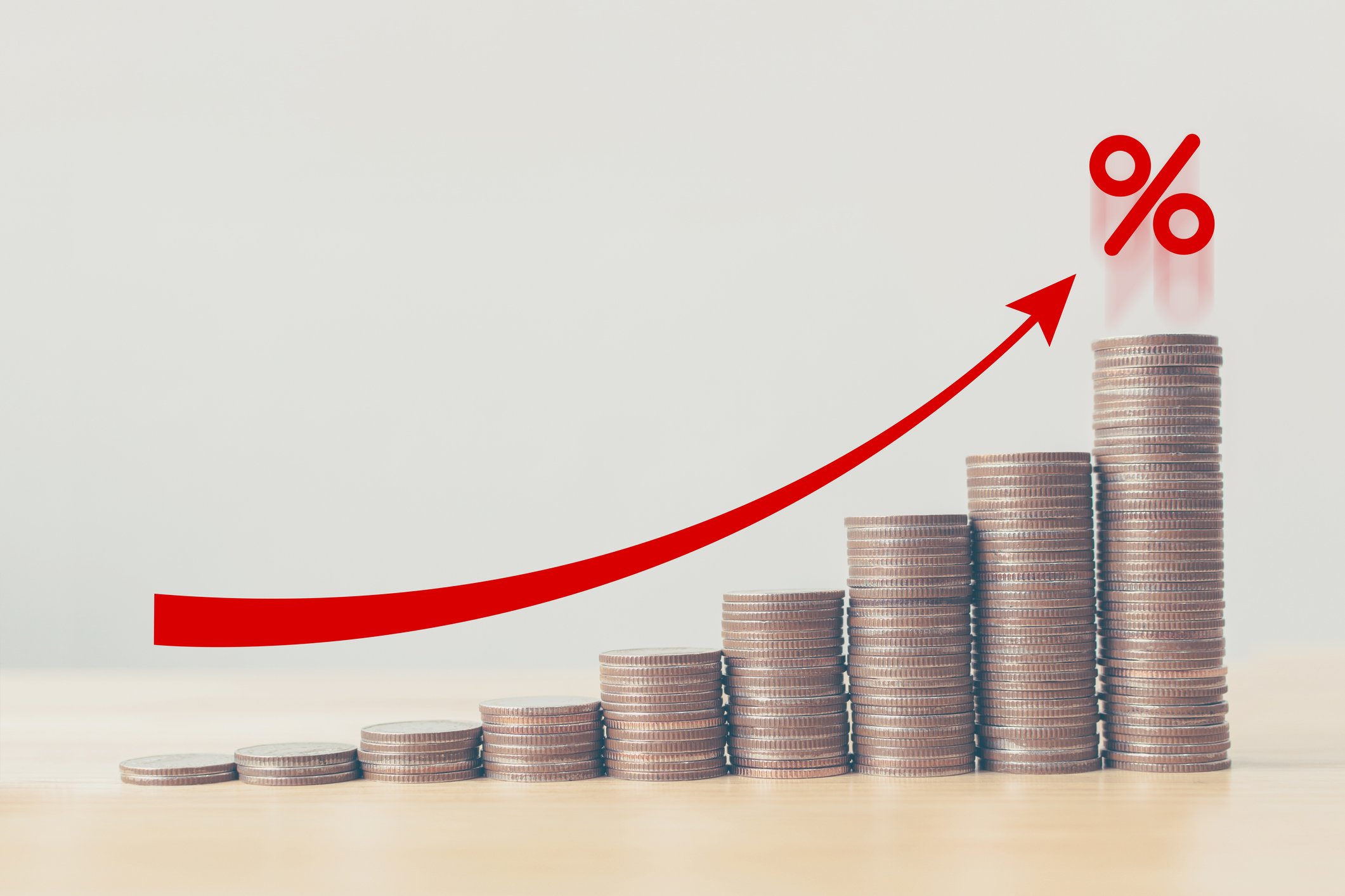 Several stacks of coins in ascending order with a red upward pointing arrow on top.