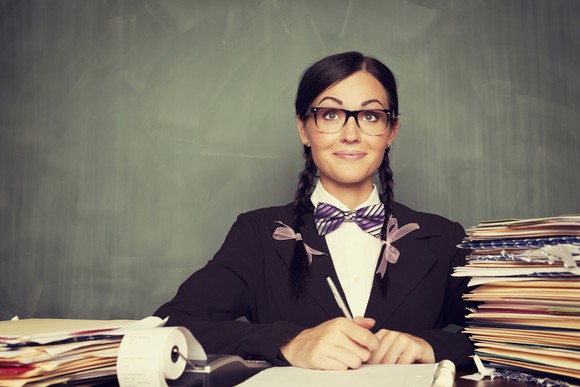 Young woman in glasses and a bowtie makes calculations  amid piles of papers. 