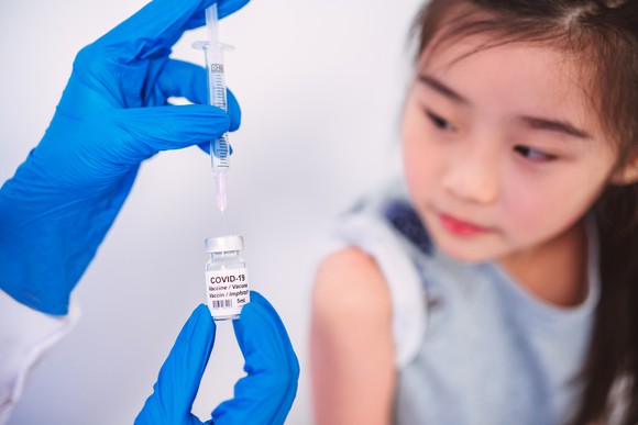 A researcher draws up coronavirus vaccine in a syringe as a little girl watches.