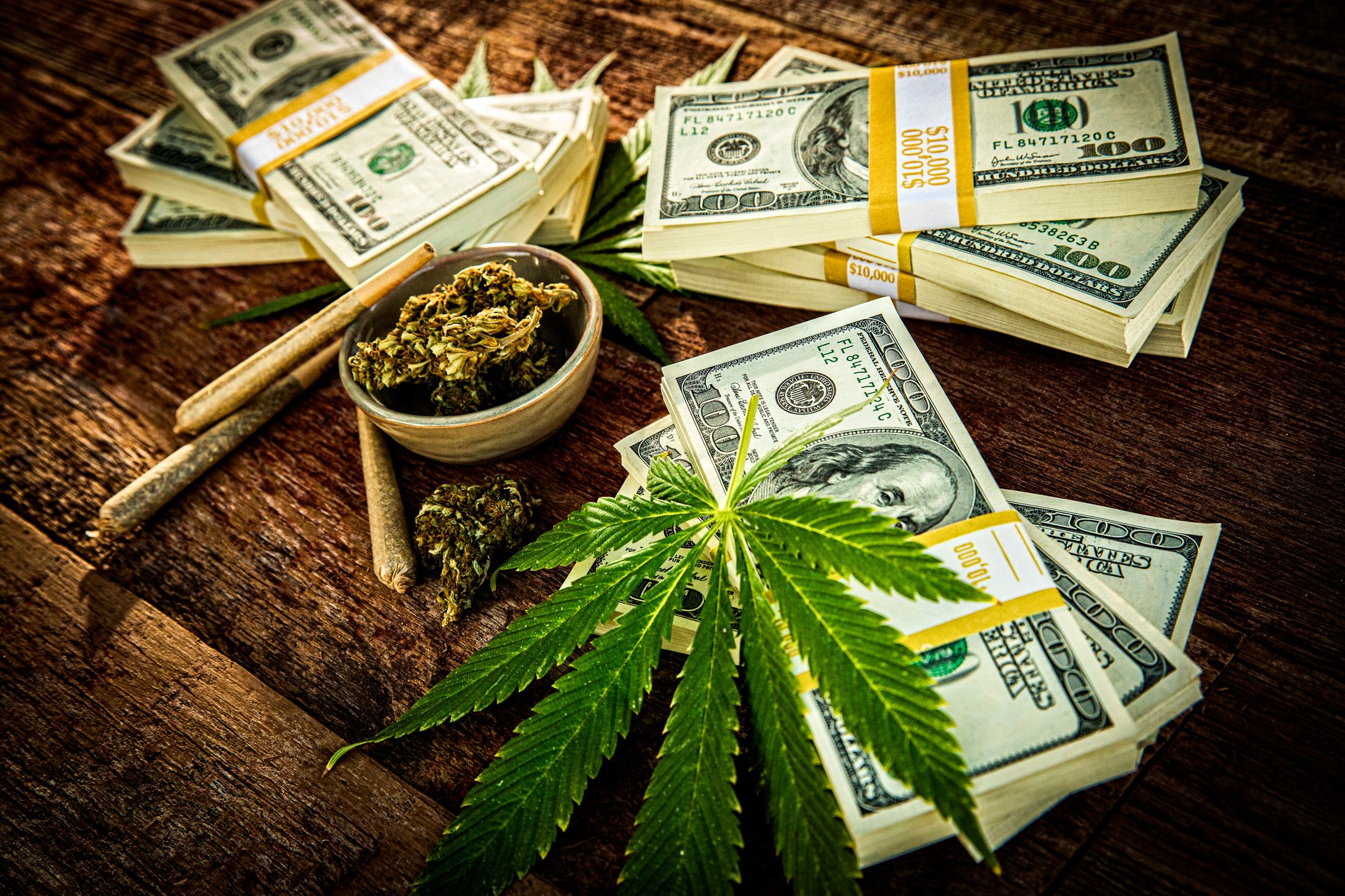 Cannabis flower buds, joint, marijauana leaf and bundles of American dollar bills.