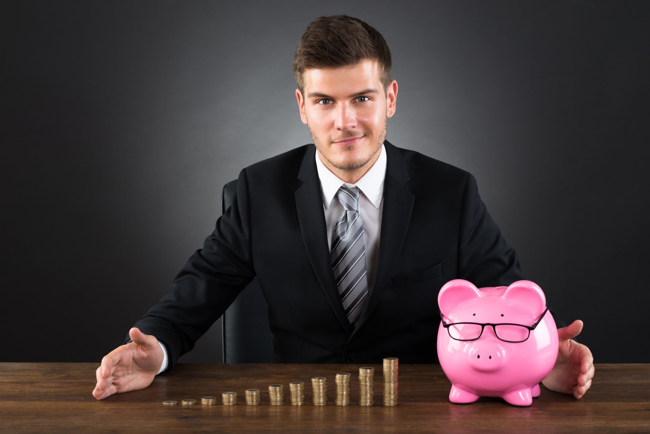 Investor with stack of coins next to piggy bank.
