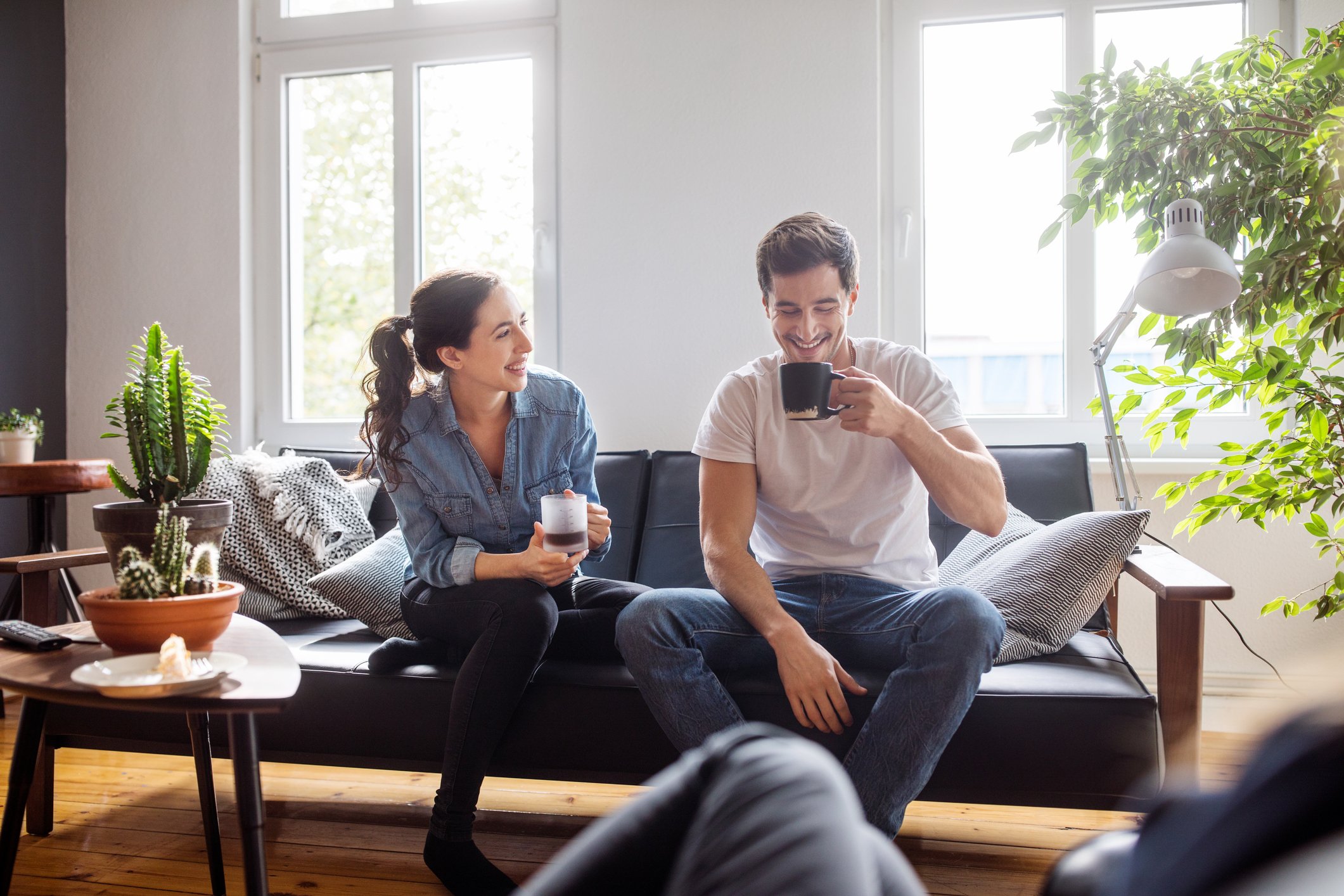 A couple drinking coffee on a couch.