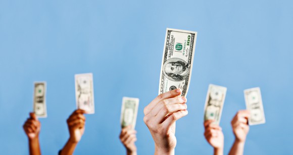 Several hands holding up bills of U.S. currency.