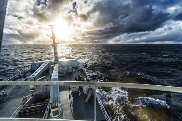 Sun breaking through storm clouds from the perspective of an oceangoing vessel.