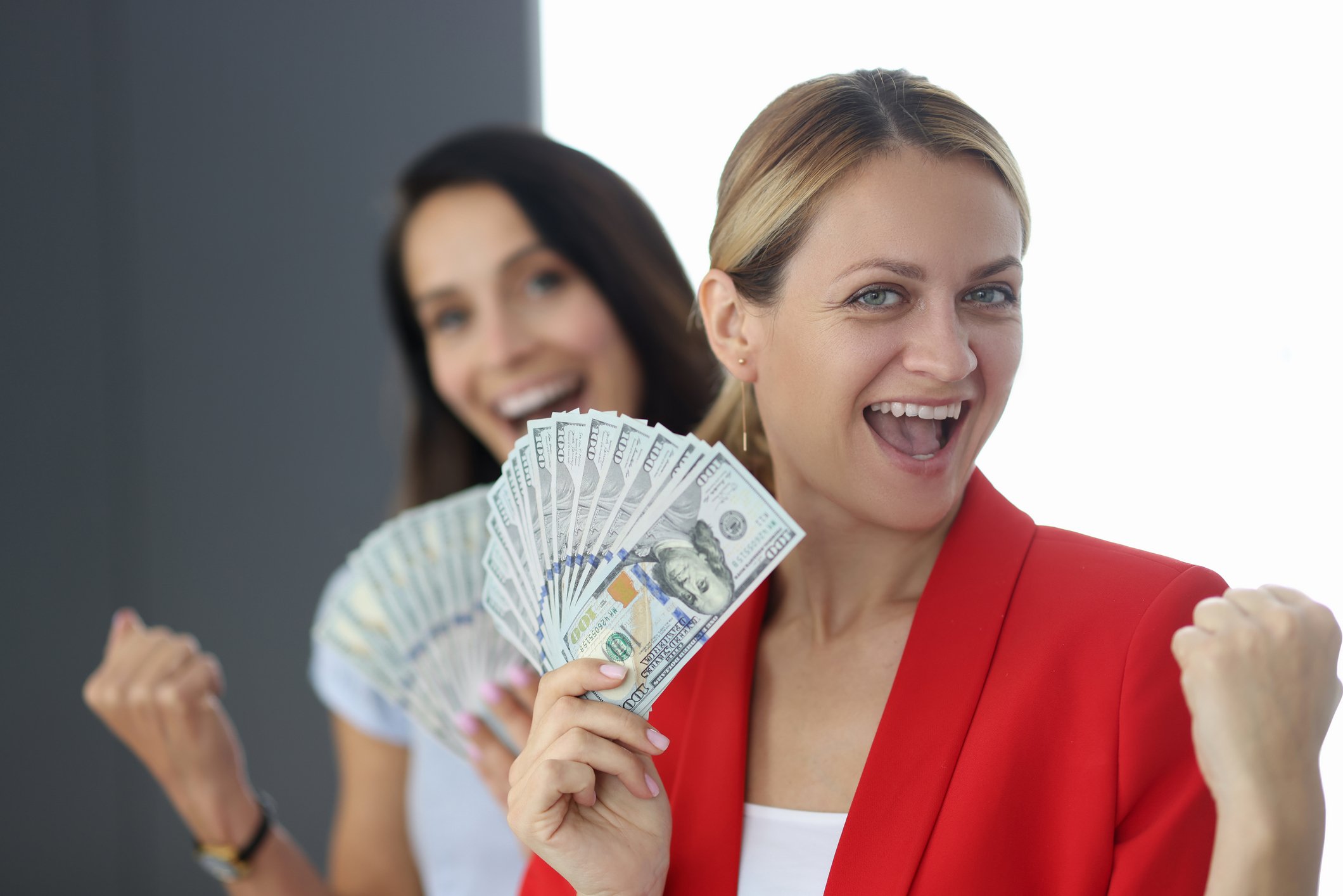 Two women triumphantly holding fanned out cash.