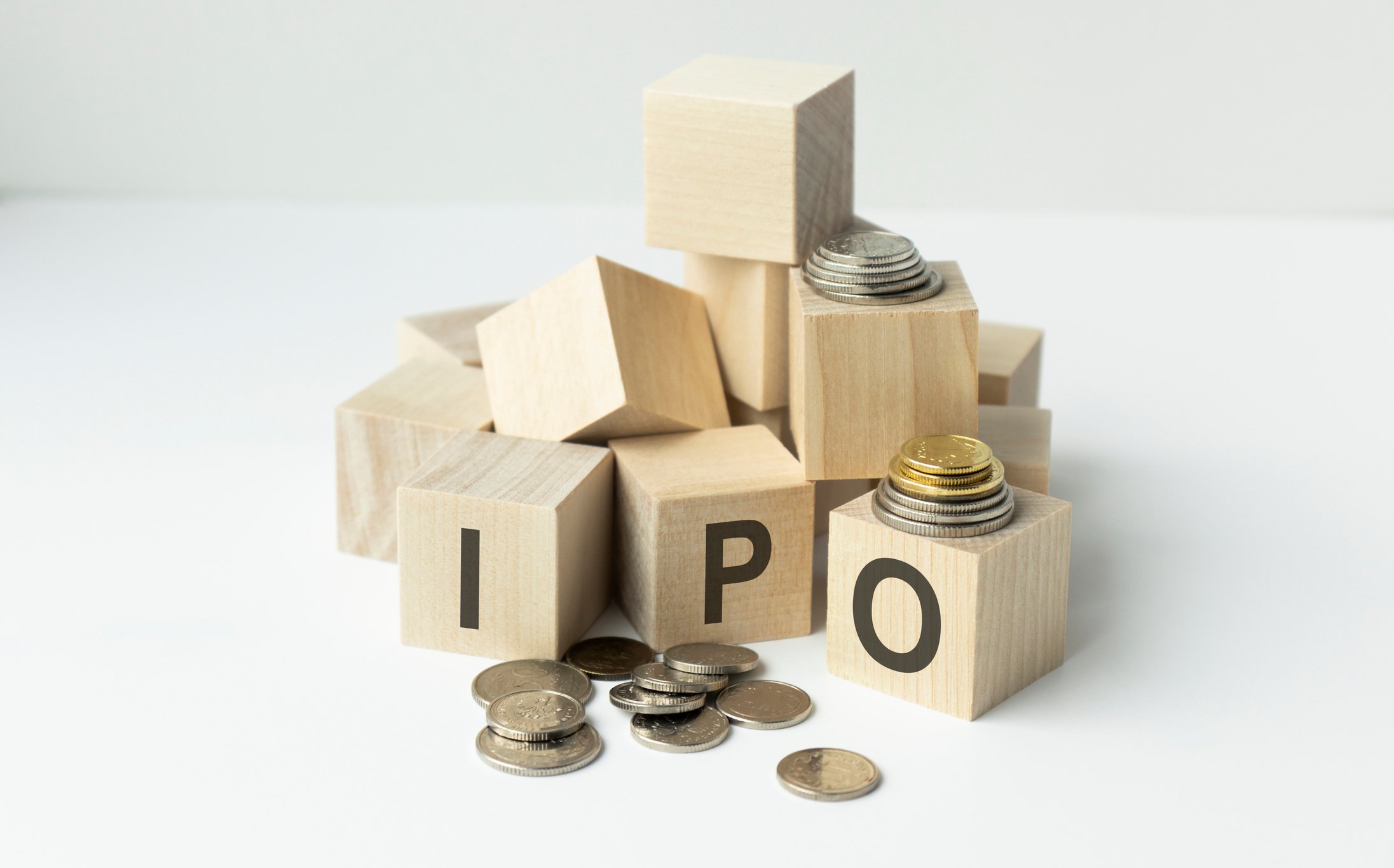A pile of wooden blocks with three spelling out "IPO," with a scattering of coins.