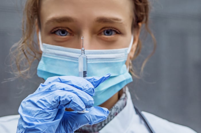 A masked and gloved nurse holds up a dose of coronavirus vaccine.