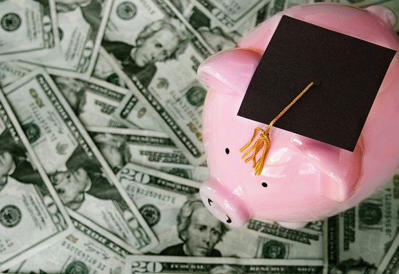 Piggy bank with a graduation cap sits on a pile of money.