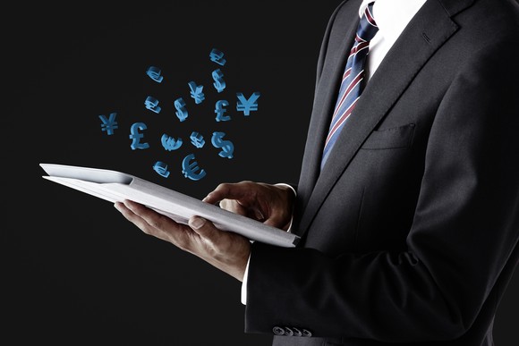 Businessman seen from neck down working a tablet with foreign currency symbols coming out. 
