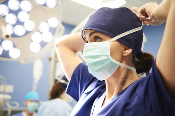 A woman in scrubs puts on a surgical mask.