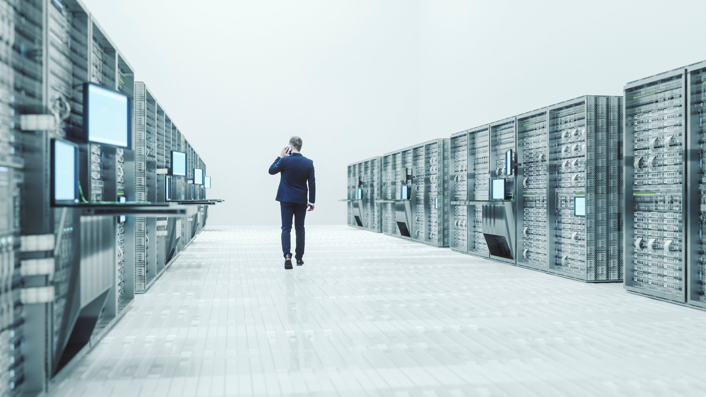 Man walsk between two rows of server racks in a big open white room. 