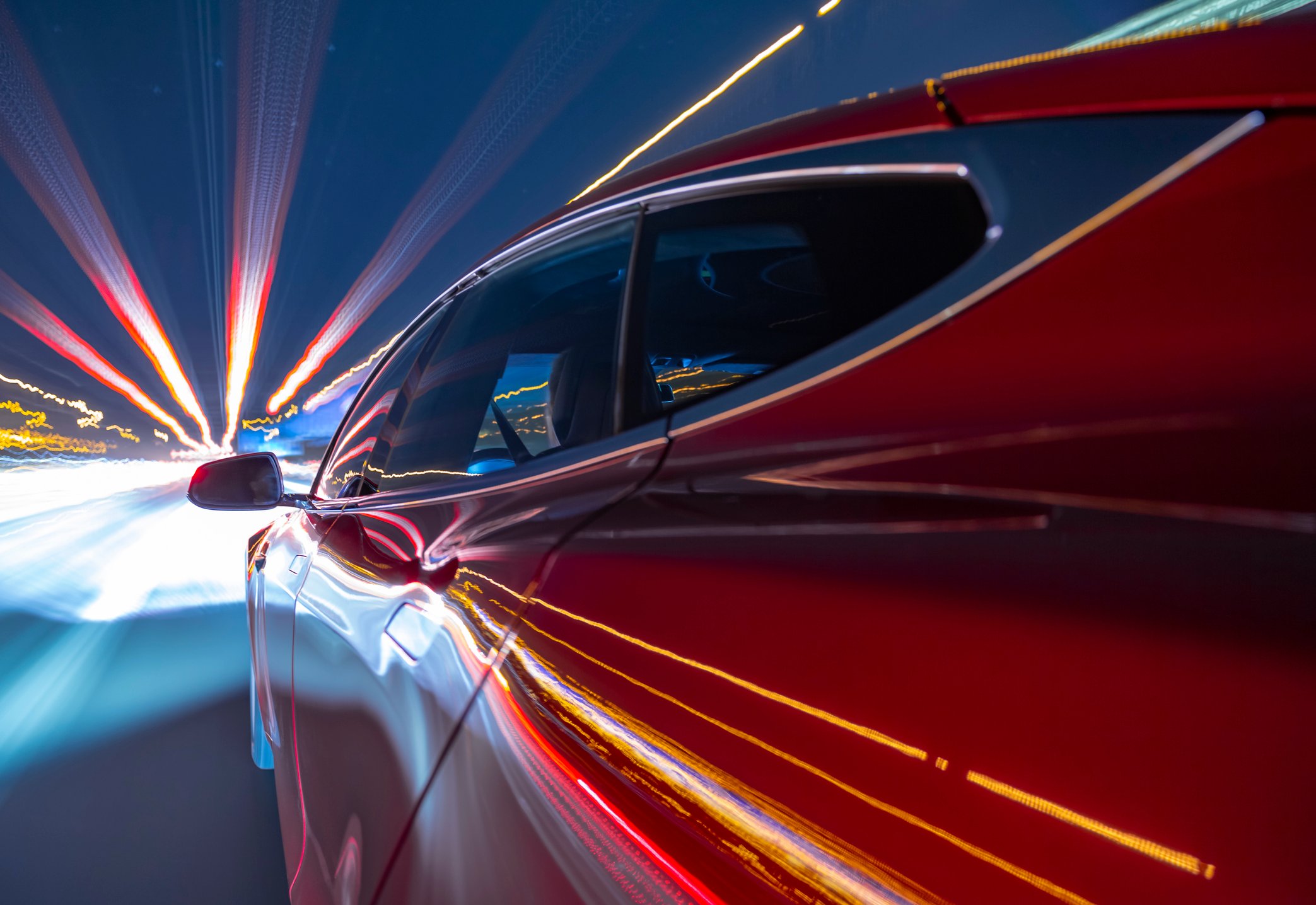 Closeup of red electric vehicle speeding on a highway at night with lights streaking by. 