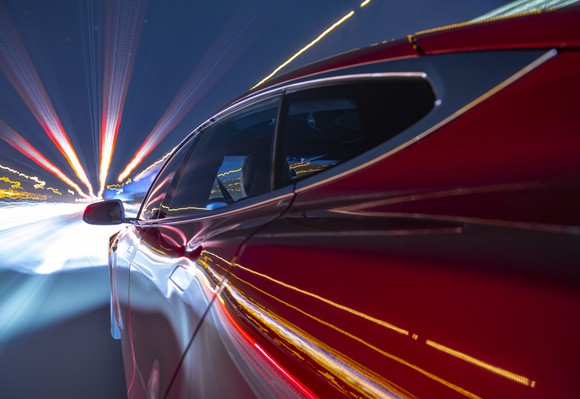 Closeup of red electric vehicle speeding on a highway at night with lights streaking by. 