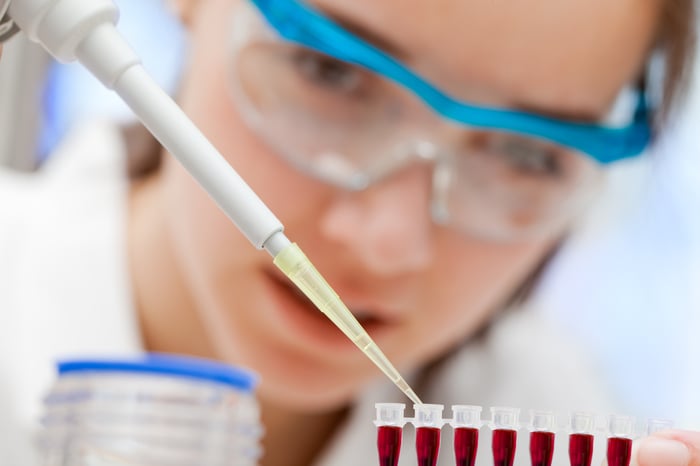 A pharmaceutical lab technician using a pipette to place liquid samples in test tubes. 