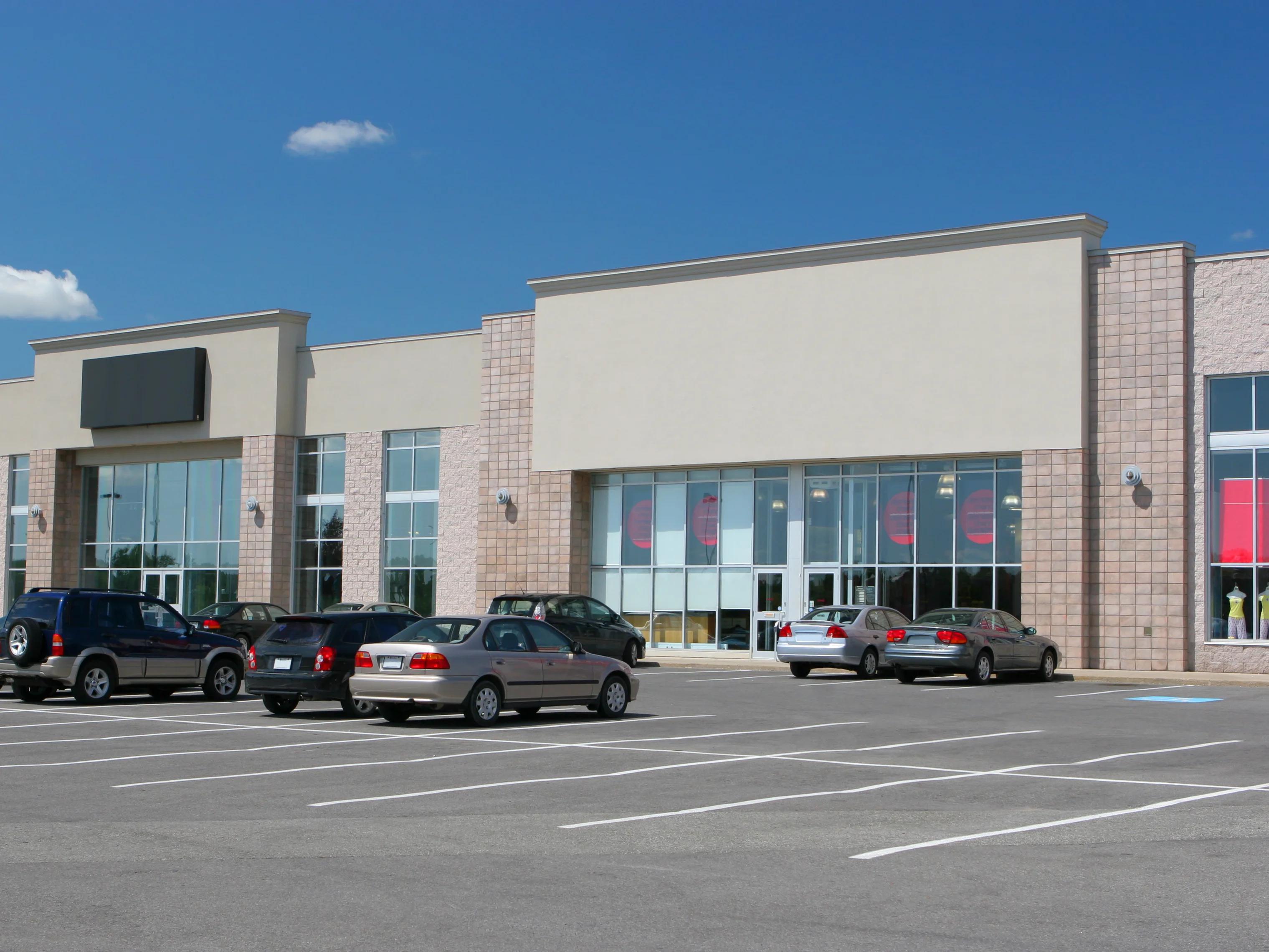 Strip mall with retail stores and some cars in parking lot.
