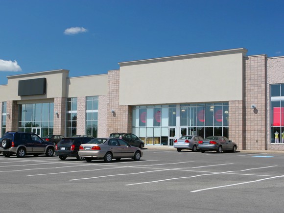 Strip mall with retail stores and some cars in parking lot.