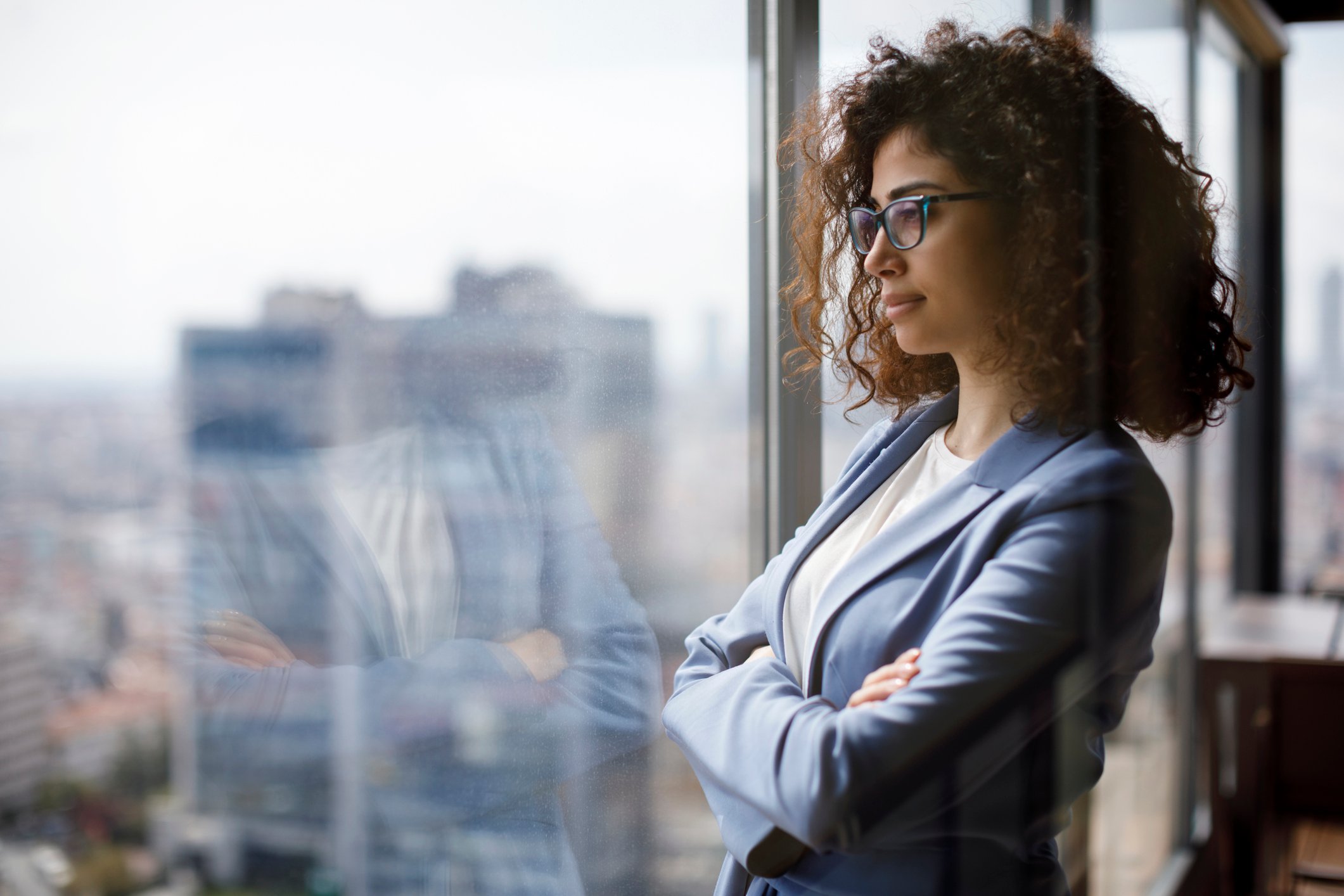 Woman wearing glasses and a suit looks out a window from a high rise.