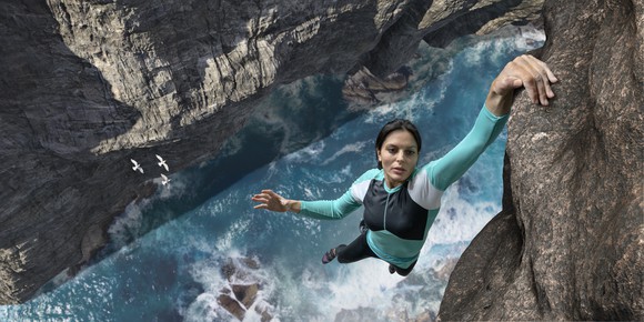 Woman hanging on the edge of a cliff with one hand above a rushing river.