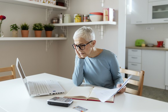 Senior woman looking at laptop and papers