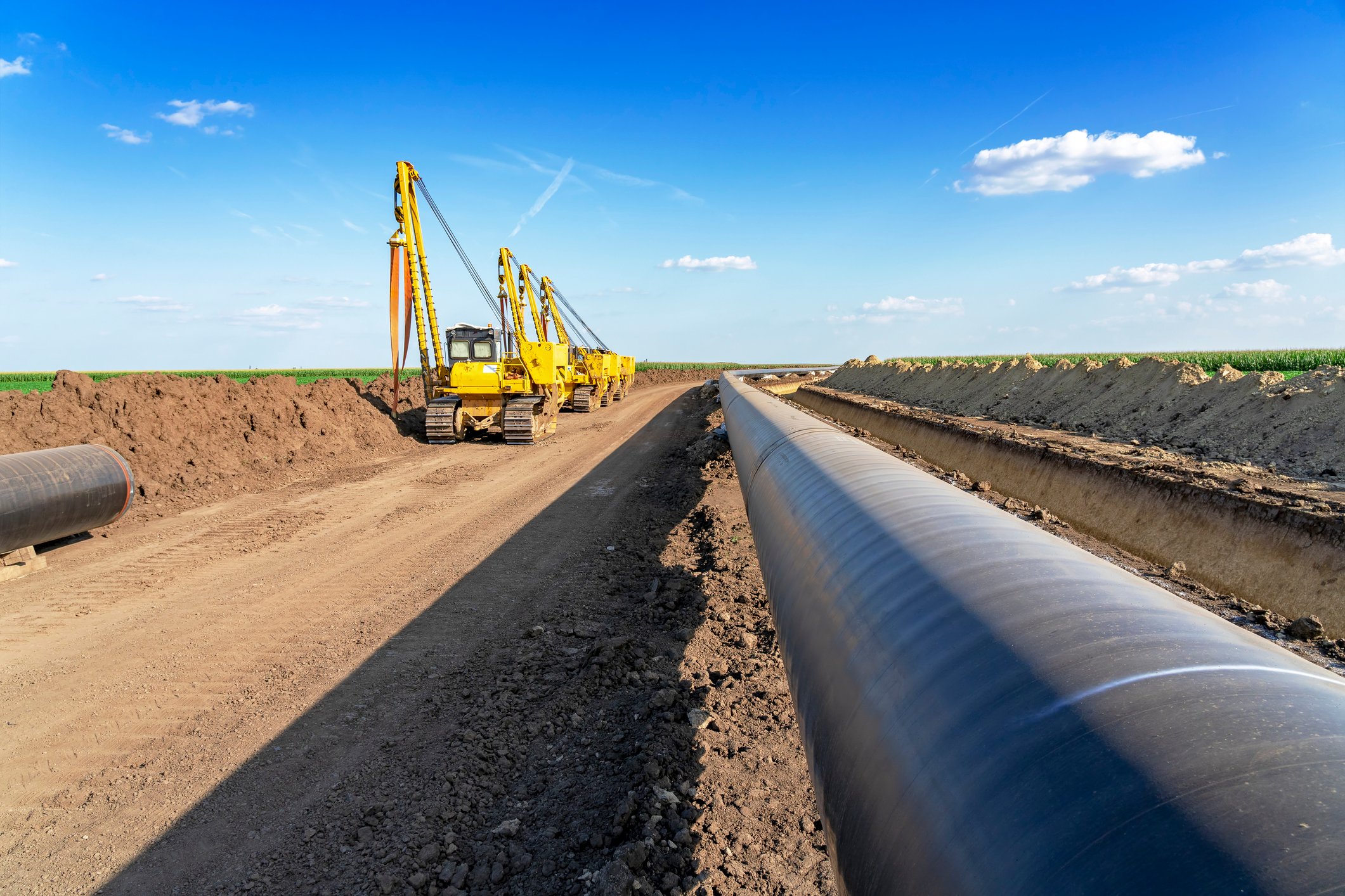 Gas pipeline along with construction equipment under blue sky. 