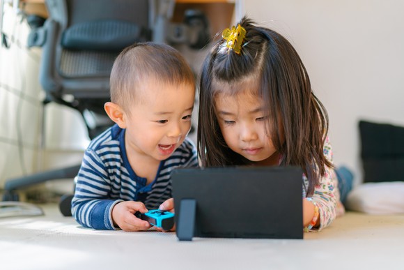 A young boy and girl playing a game together on a tablet.