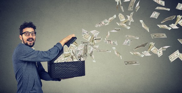 Dollar bills flying out of a box held by a young man.