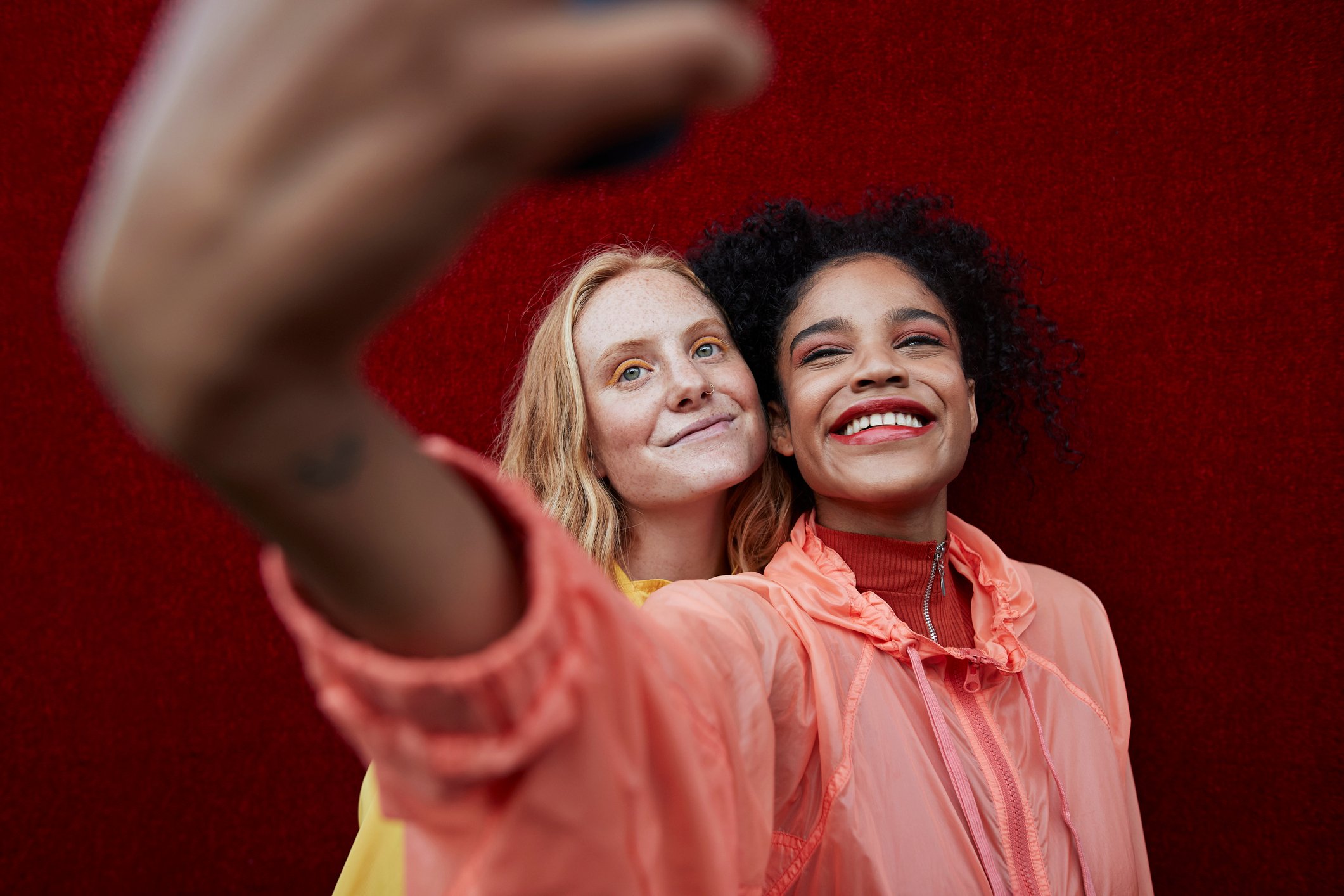 Two women take a selfie against a red wall. 