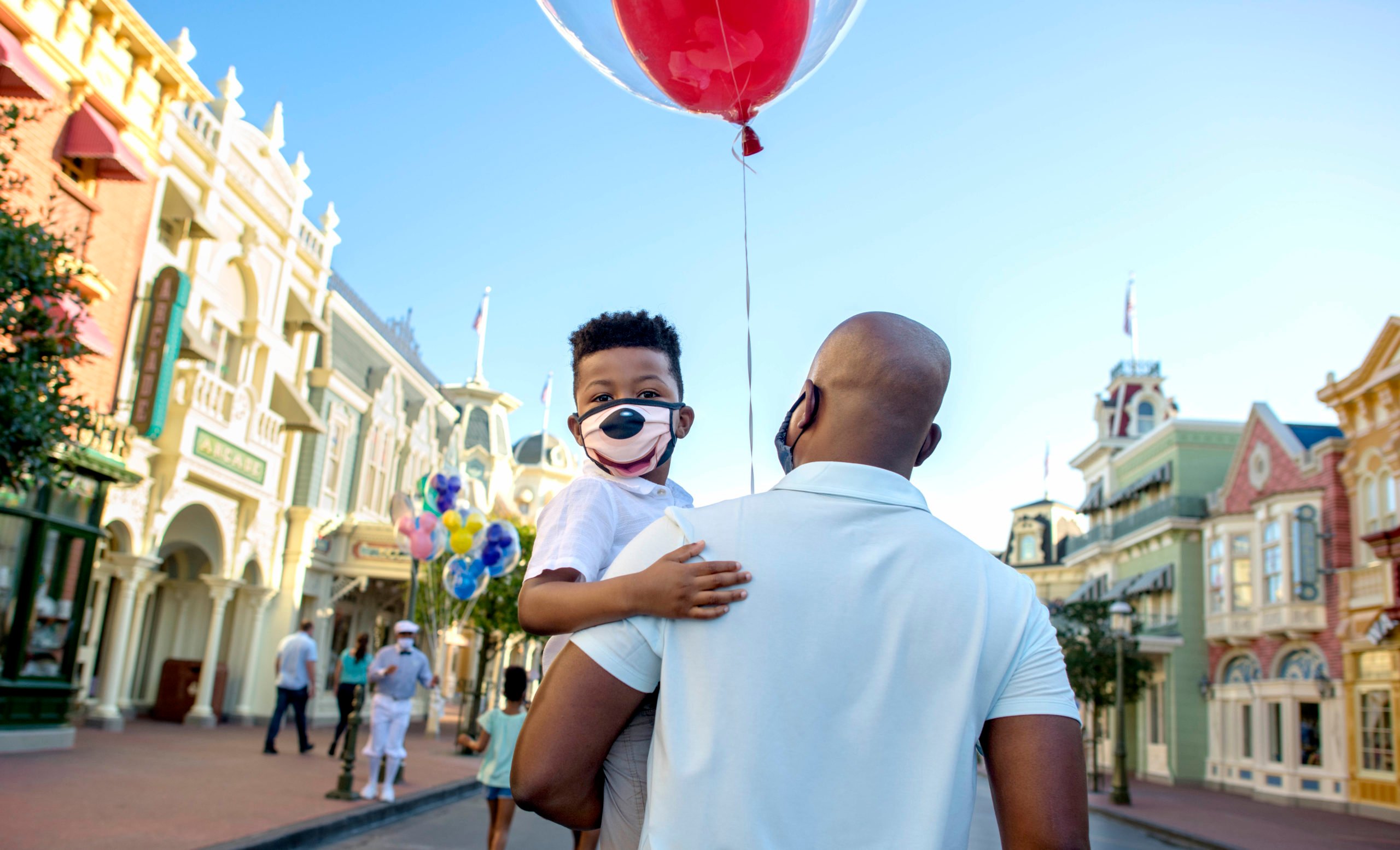 A dad holds his masked son as the walk in Disneyland.