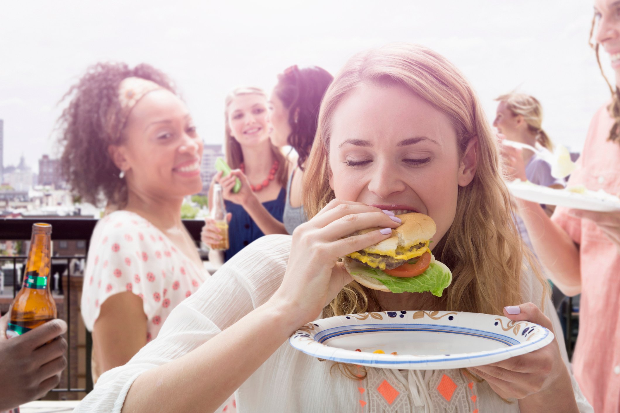 Friends stand on a deck smiling and eating veggie burgers.