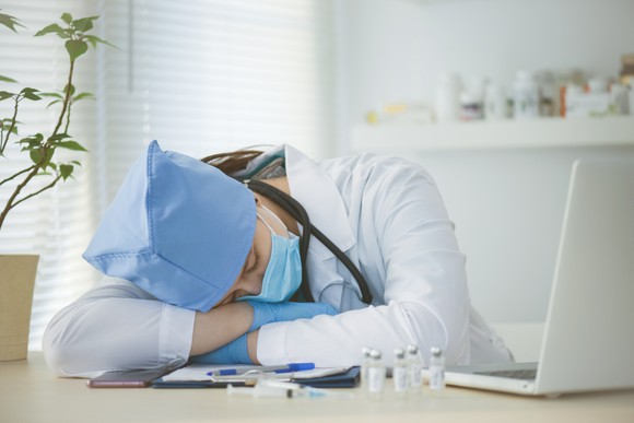 Exhausted healthcare worker rests on desk with several vials and syringes 