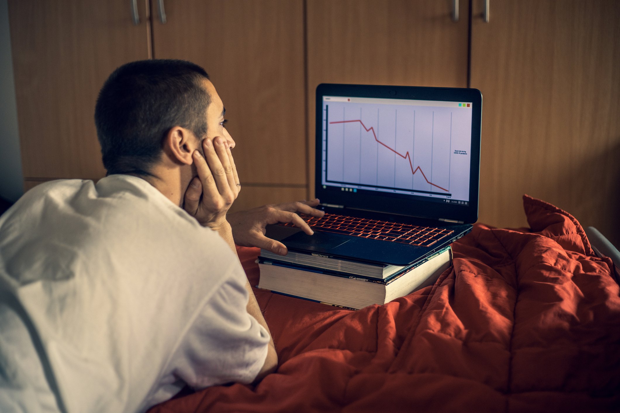 Man with head in hand looking at computer screen showing stock chart going down.