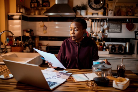 A woman looking at her computer with pieces of paper scattered around a table.
