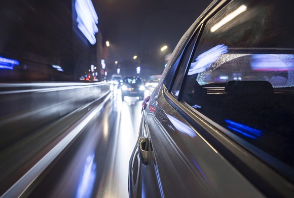 Cars zooming down a city street at night.