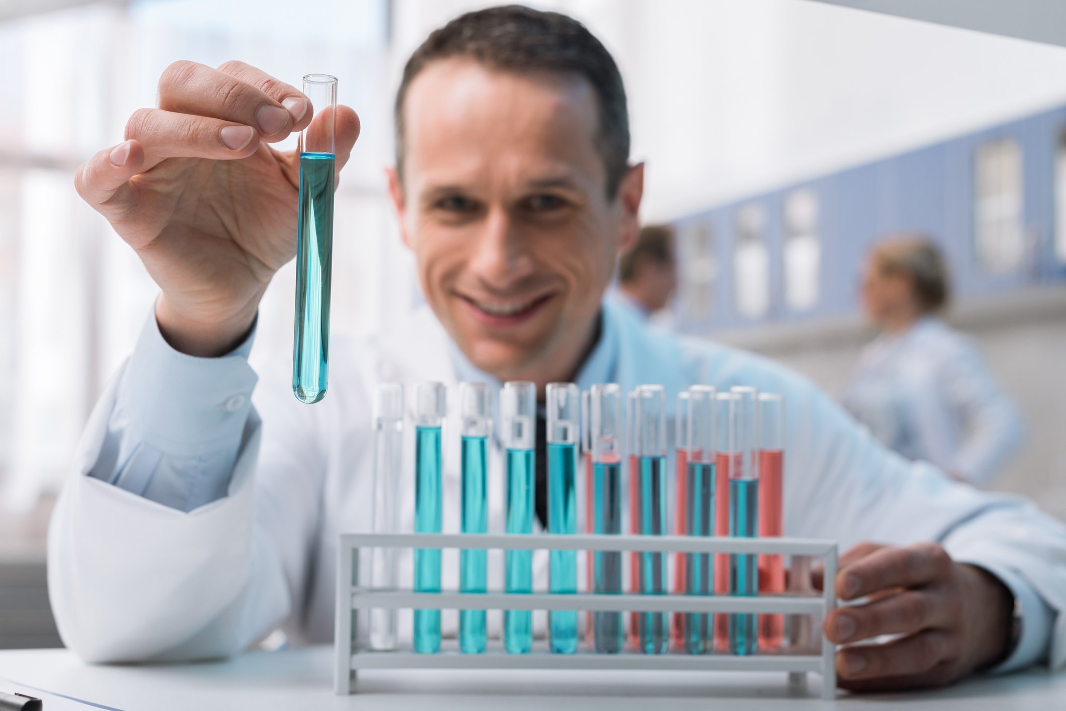 Scientist holding a test tube up with a rack of test tubes in front of him