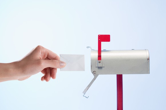 A hand reaching a letter into a small mailbox.