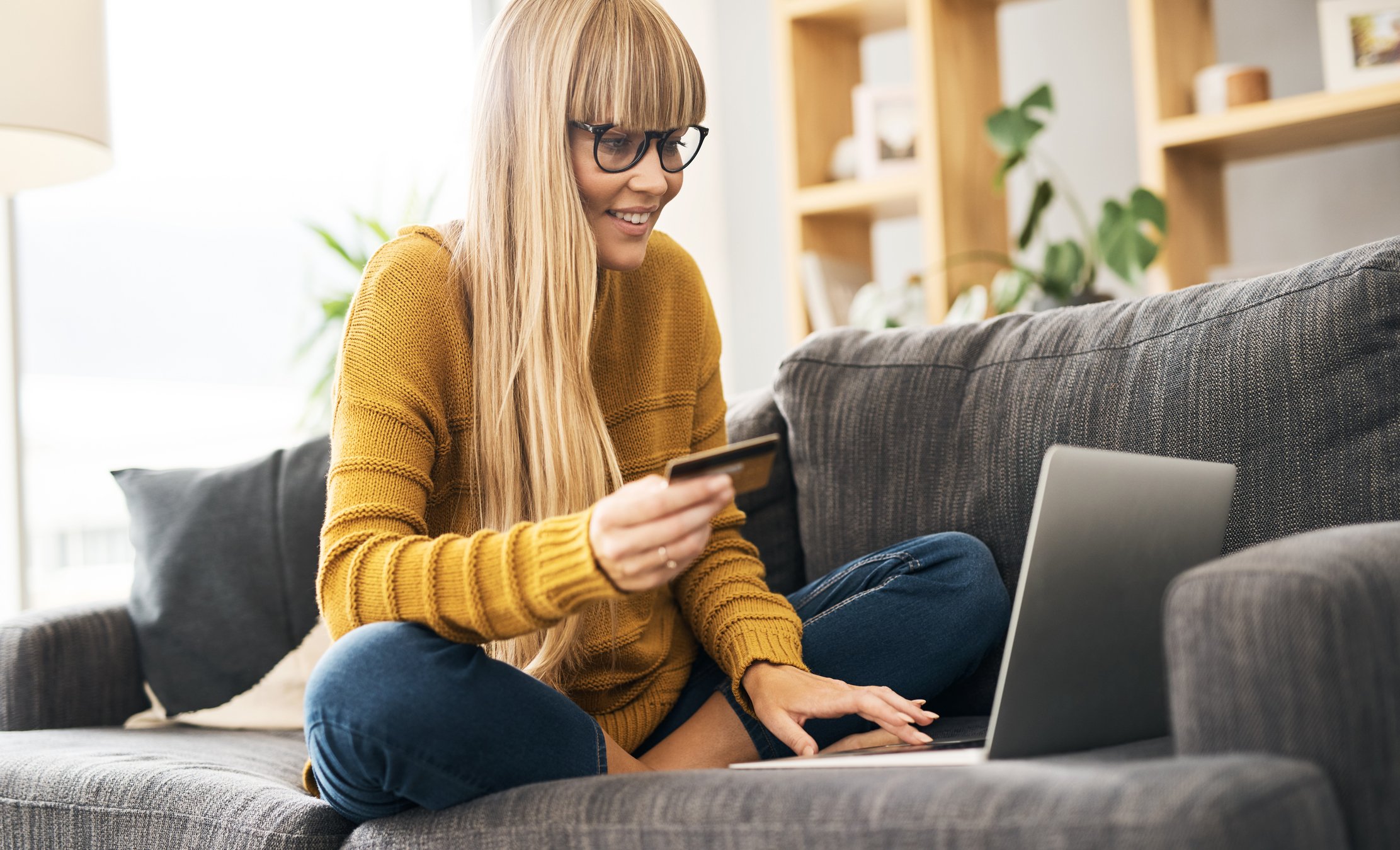 A woman sits on her couch with her laptop and shops online.