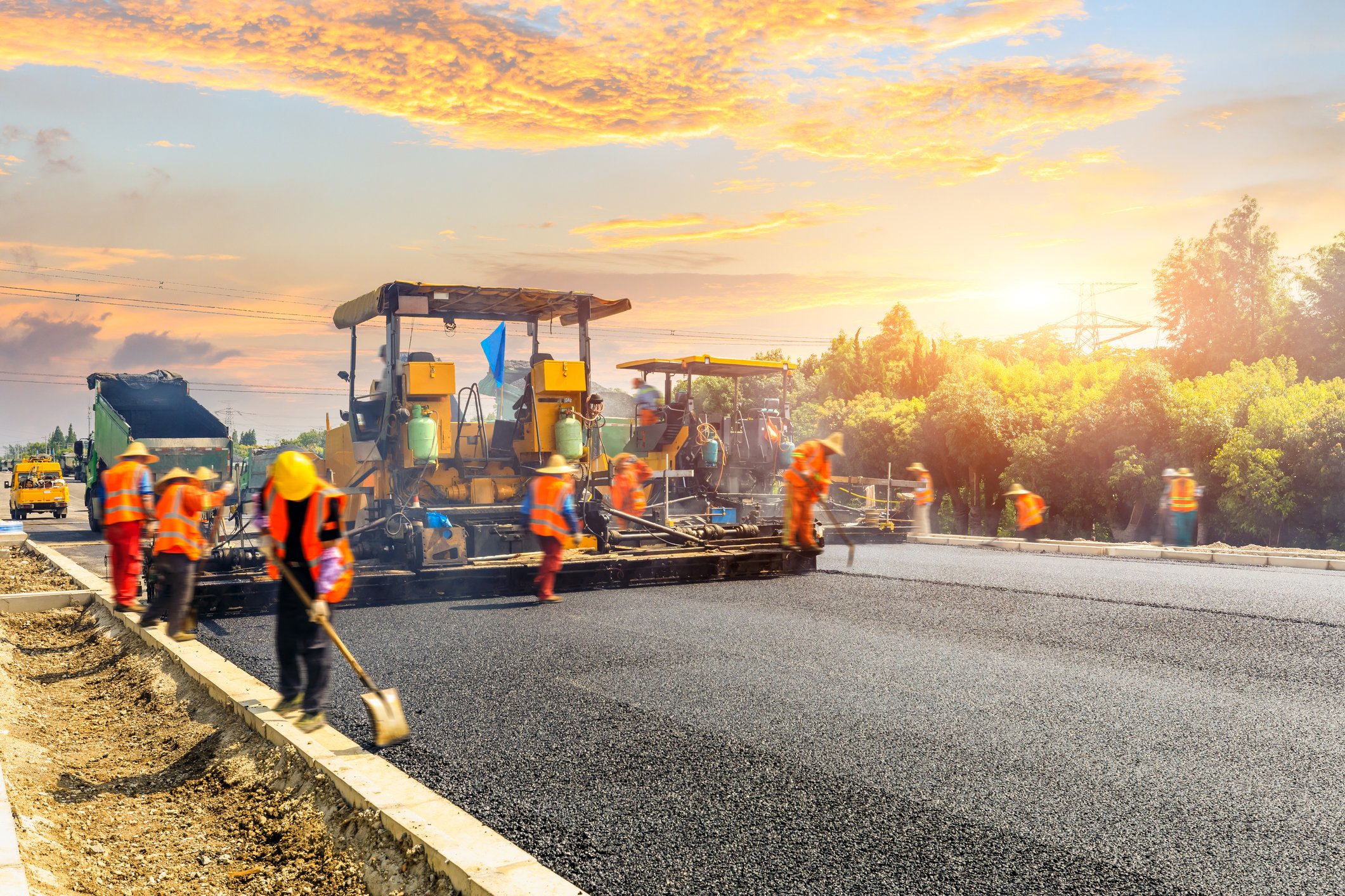 A construction crew works on a black asphalt road.