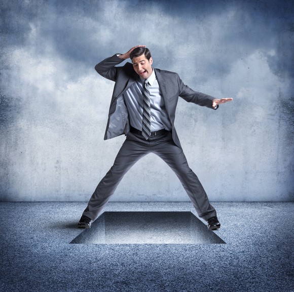 A businessman standing over a trap door