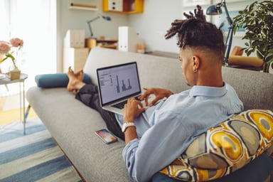 man sits on couch looking at chart on laptop