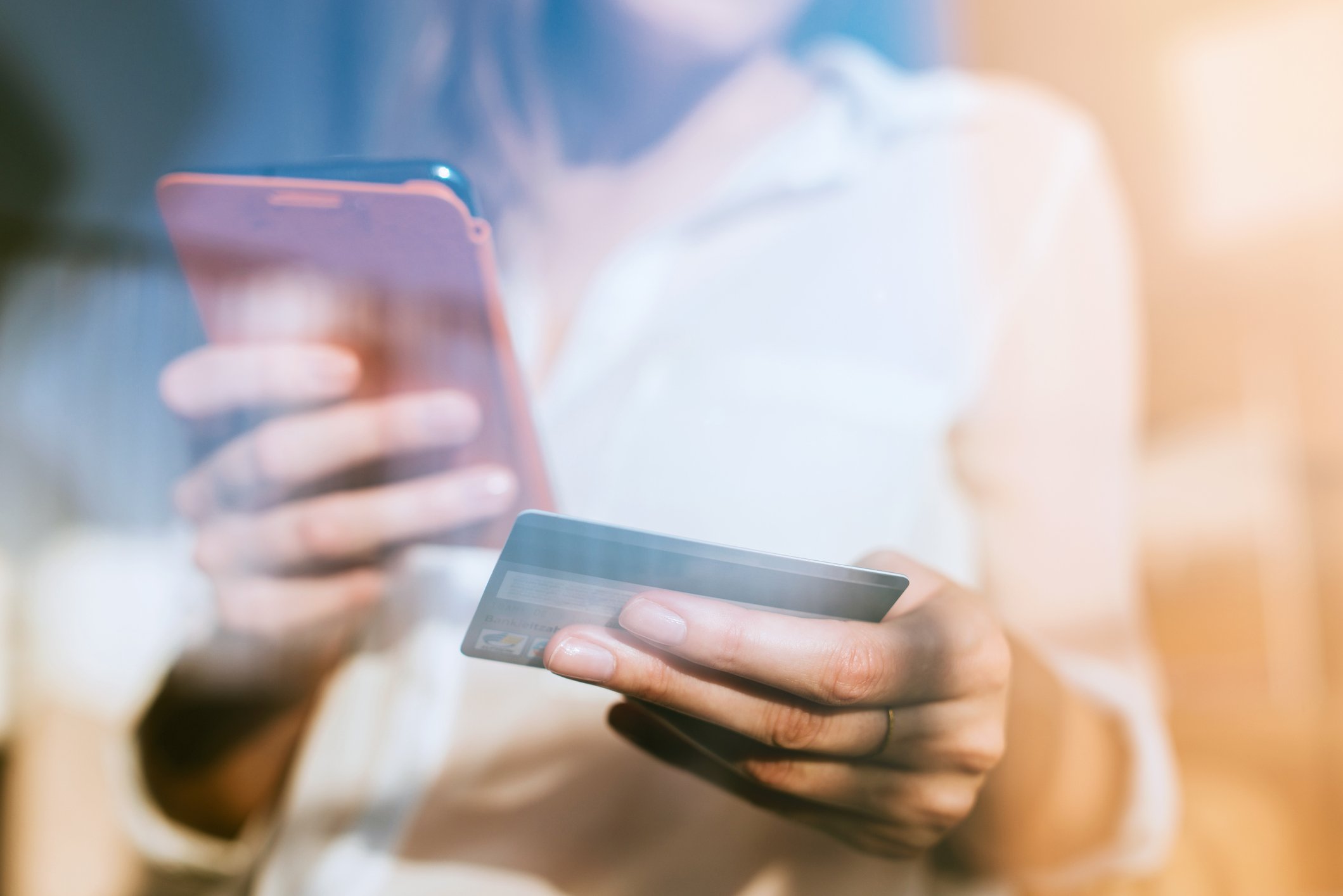 Woman holding a smartphone and payment card in separate hands.