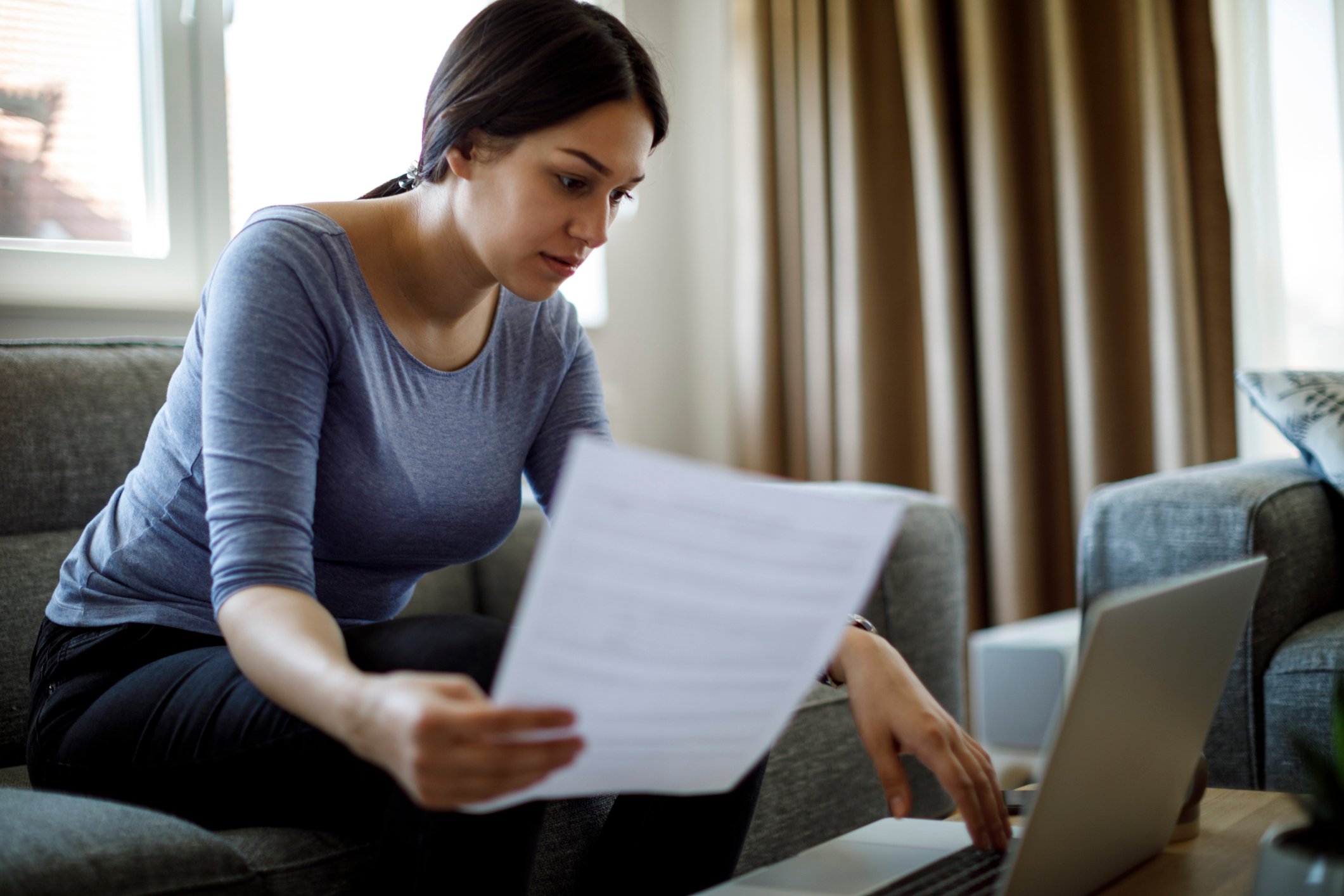 Young woman sits on couch and works on her computer.