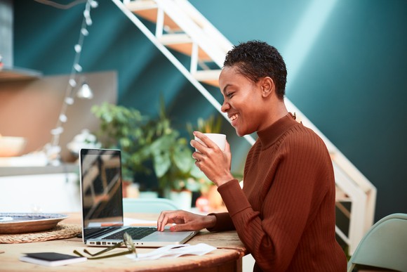 A woman drinks coffee while using a laptop