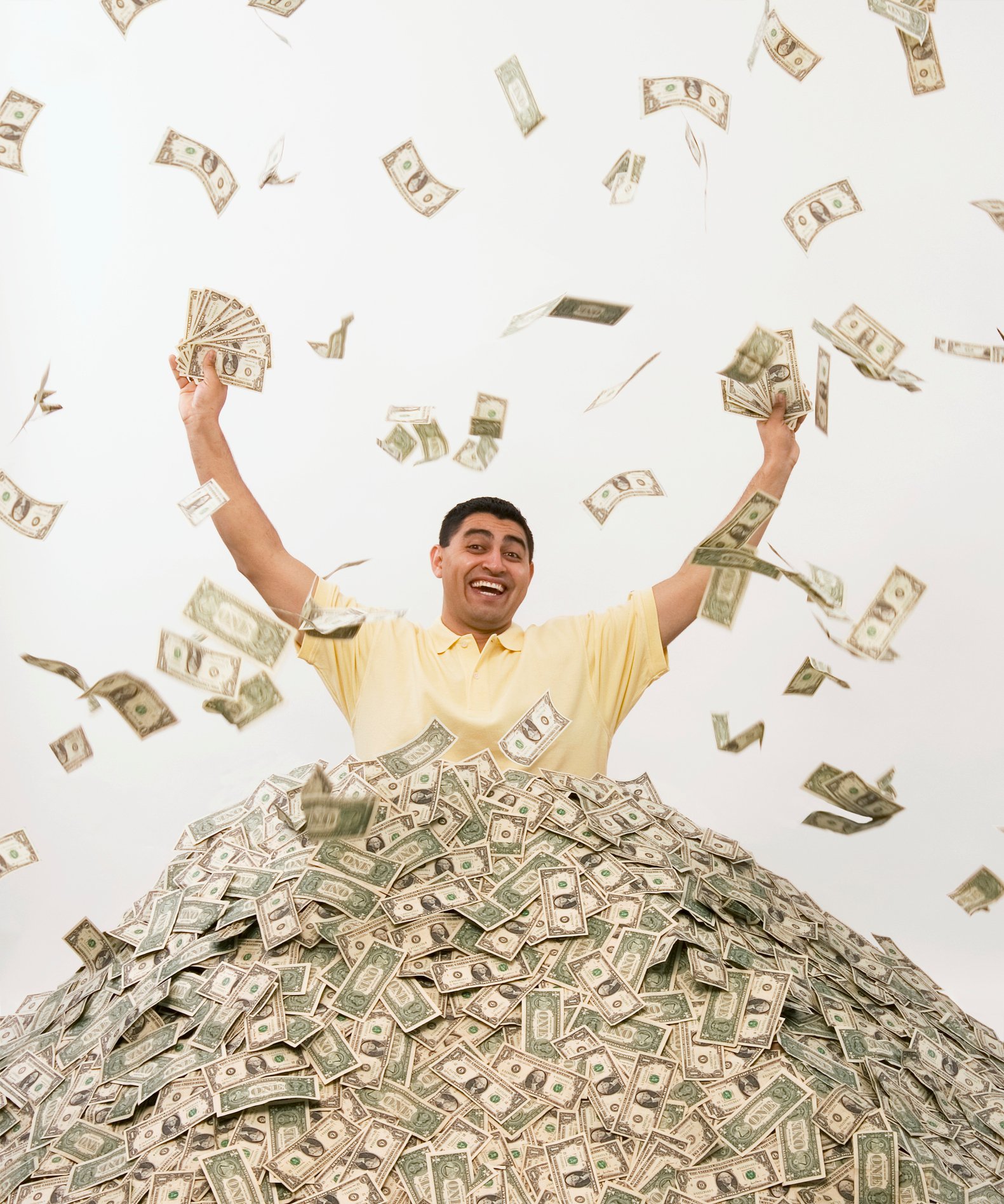 A man buried in cash holds his hands up as cash falls from the sky.