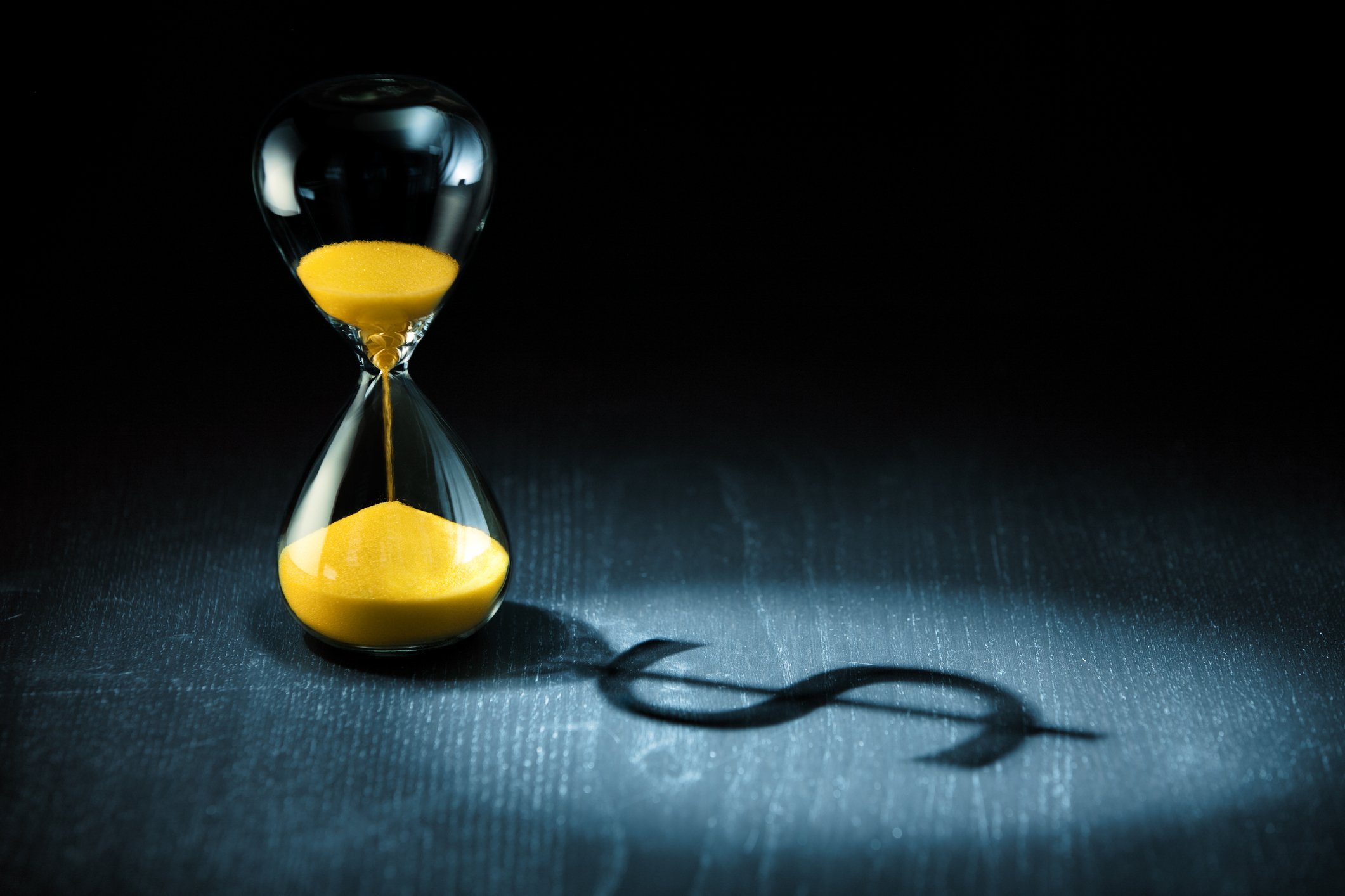 An hourglass casting a dollar-sign shadow.