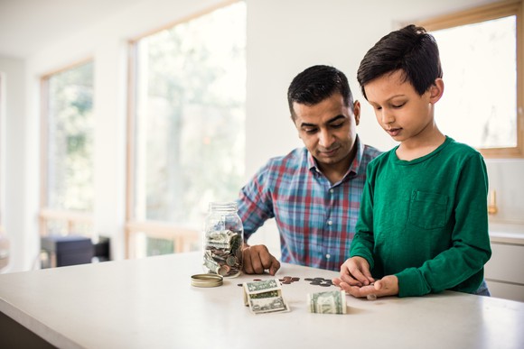 Father and son sit at a countertop and count money at home.