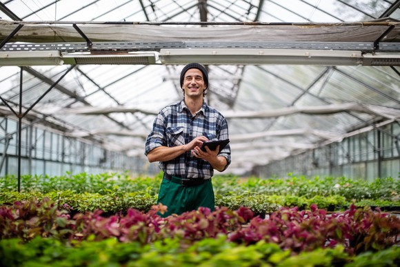 Man standing in greenhouse holding tablet and smiling
