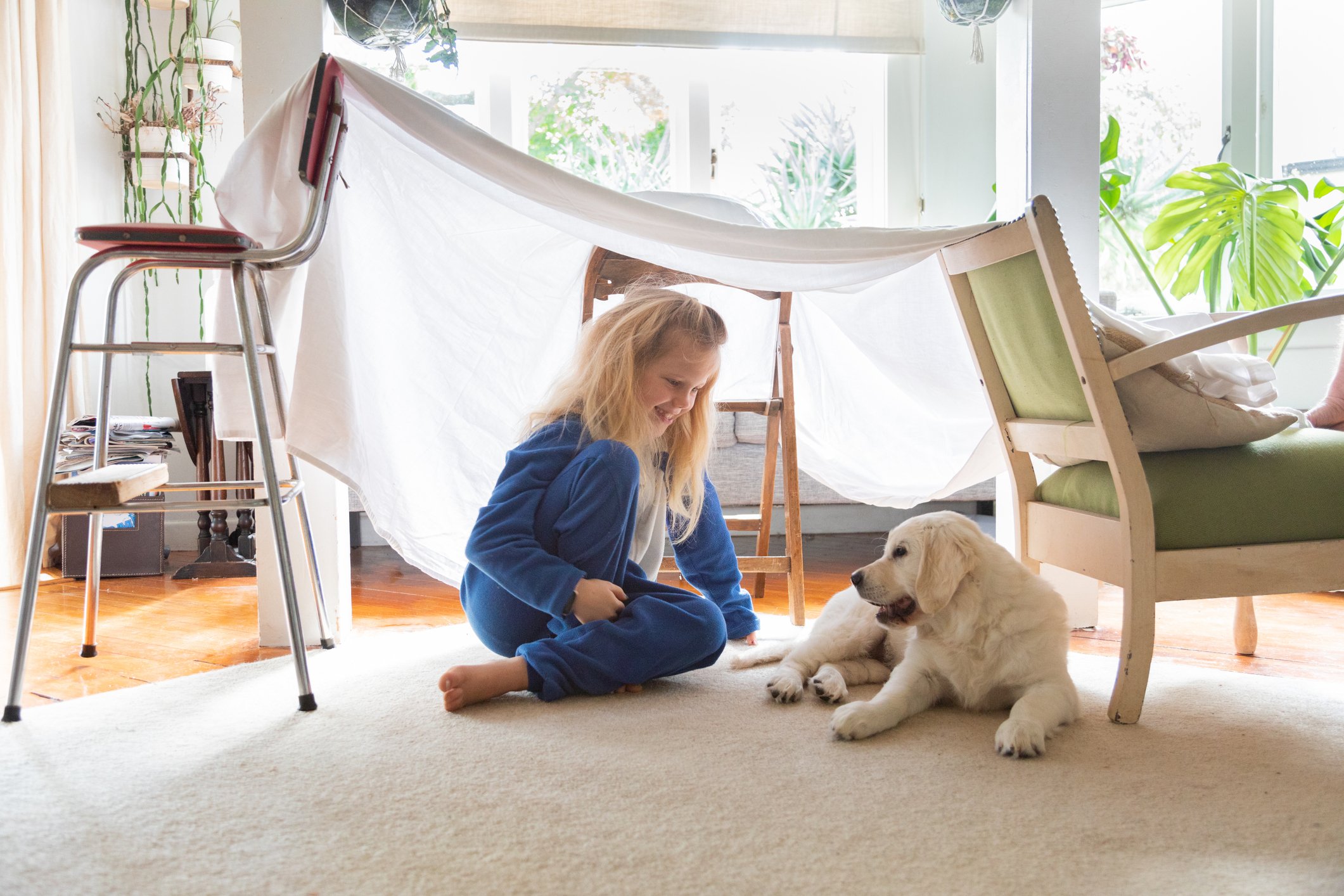 girl in indoor makeshift fort playing with puppy