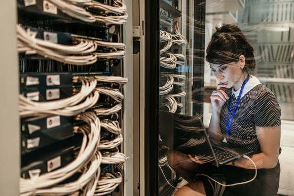 Young woman inside a data center monitoring servers on her laptop.
