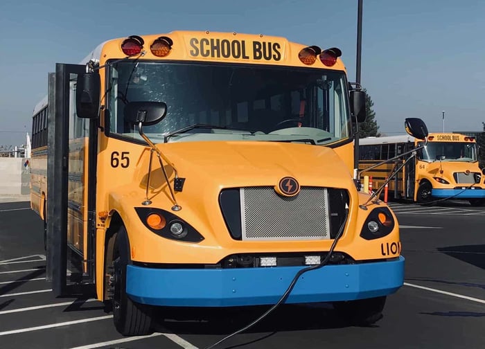 An electric school bus made by Lion Electric, shown charging in a parking lot. 