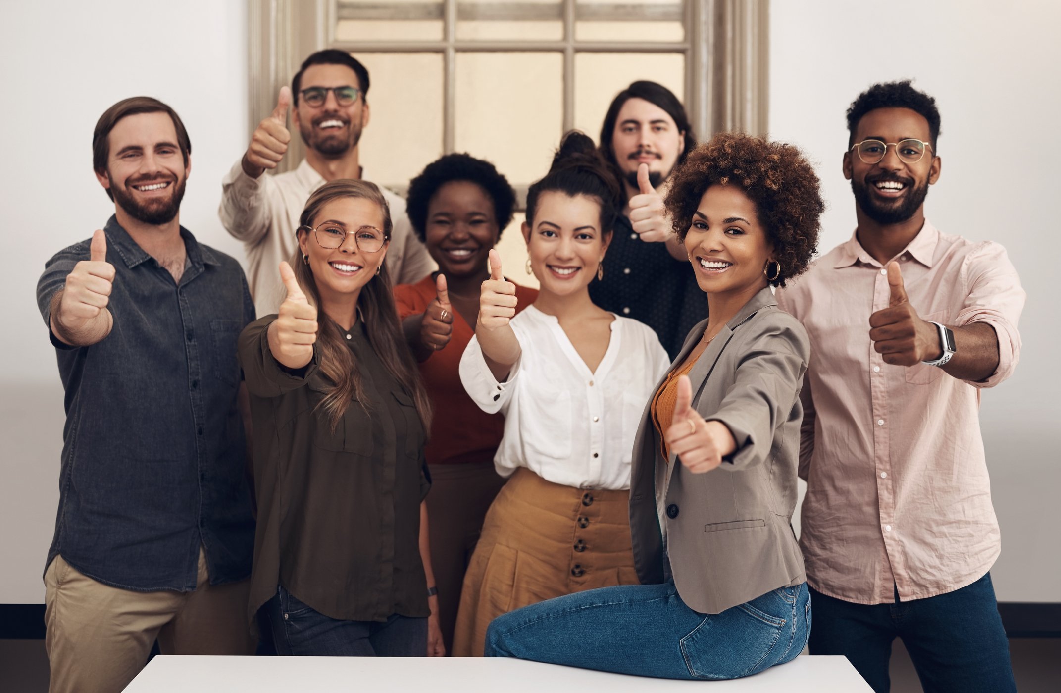 A diverse, happy workforce all give a thumbs-up sign.